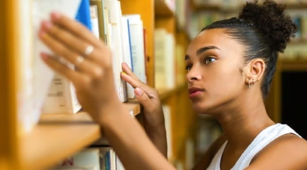 Young woman taking a book down from a library shelf