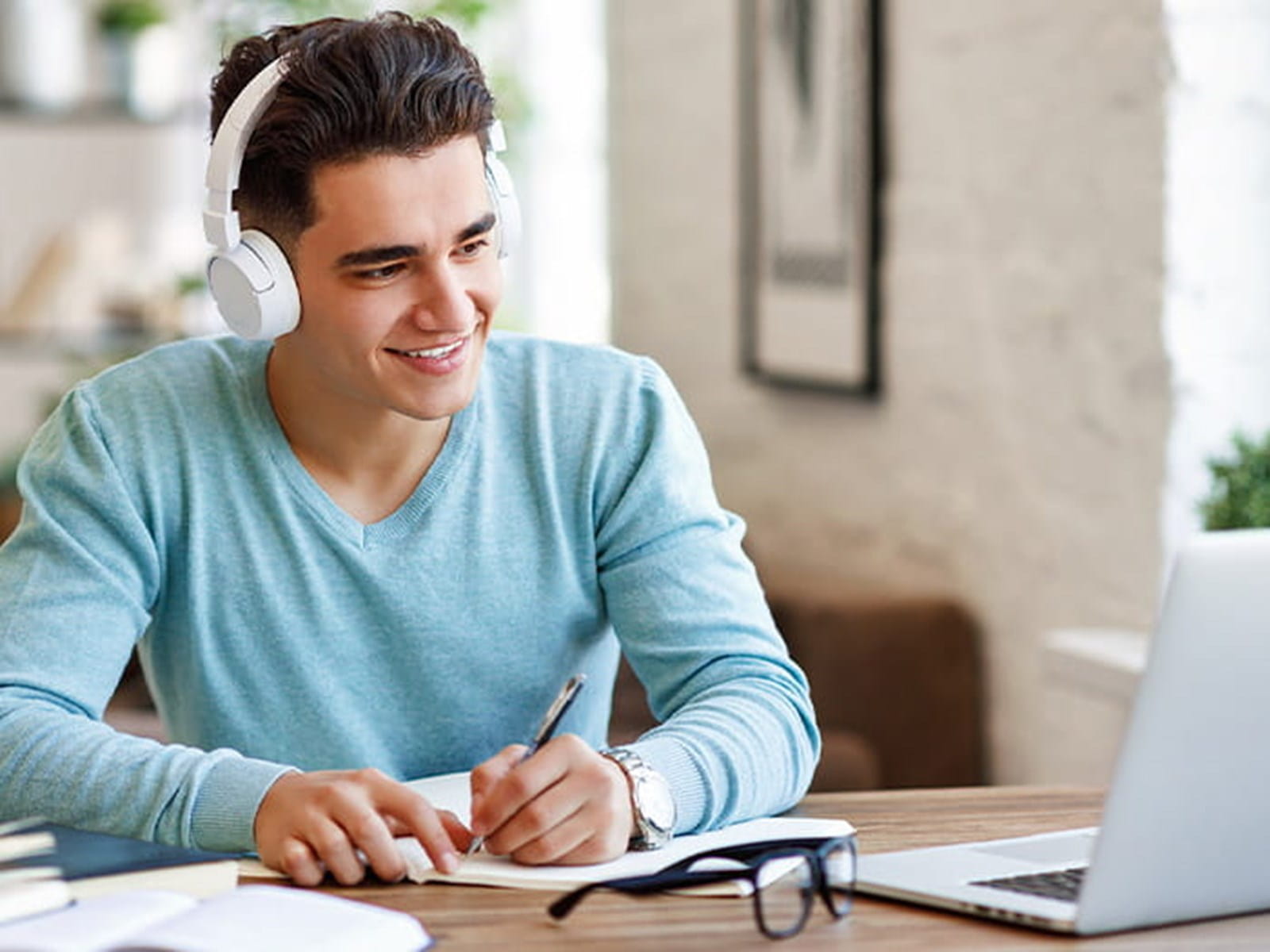 young man student studying looking at laptop wearing headphones writing taking notes