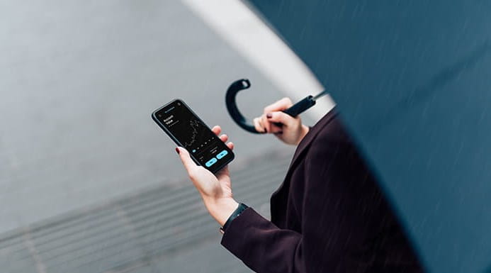 Businessperson with umbrella checking stock market on phone