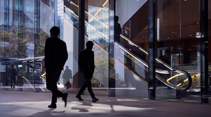 Silhouettes walking with an escalator behind them