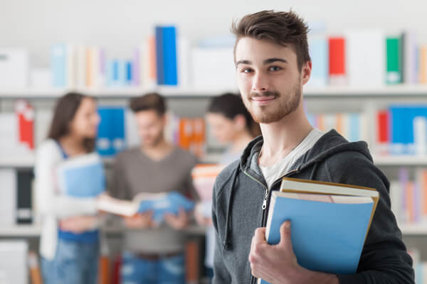 Student holding books and smiling at camera